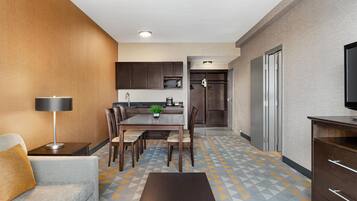 A modern hotel room with a dining area, kitchenette, and a TV on the right.
