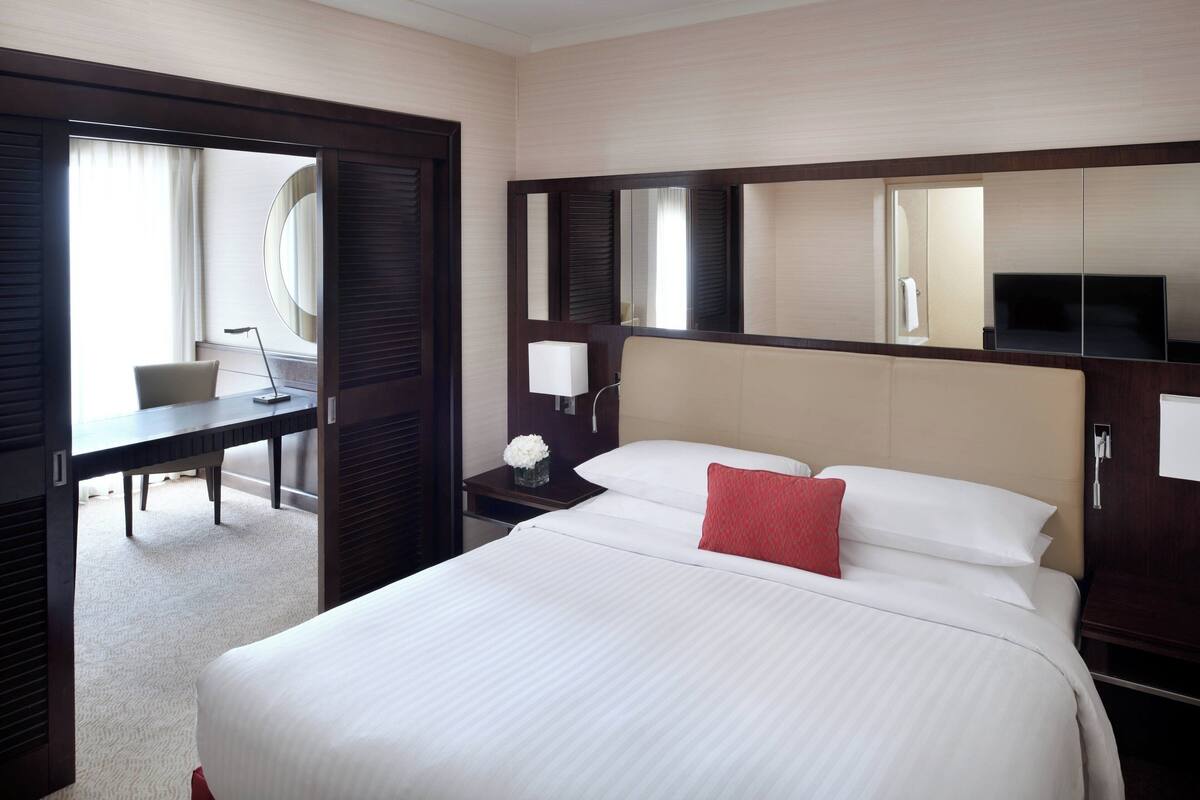 Habitación de hotel con una cama grande, un escritorio, una silla, un televisor y un espejo.
