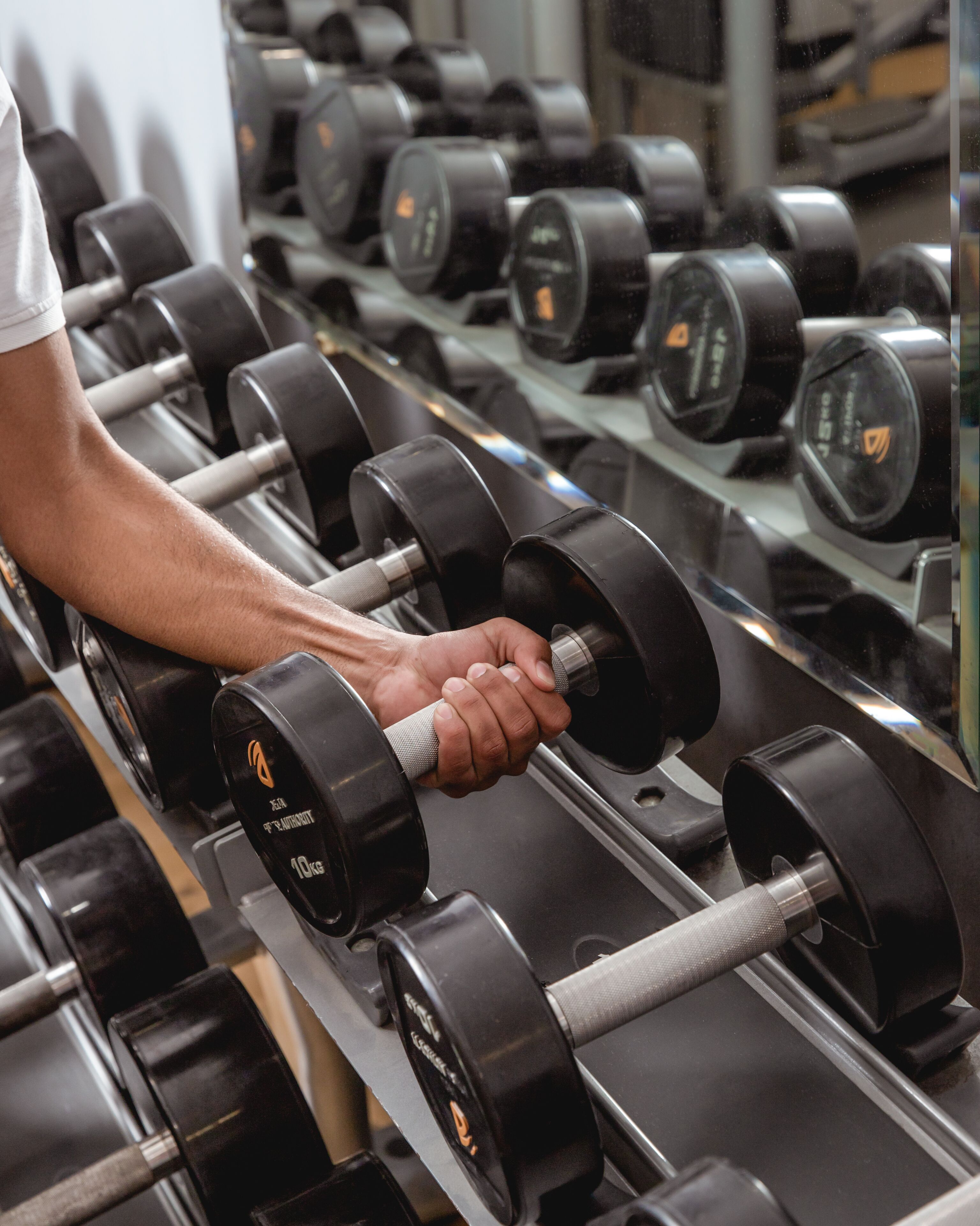 Uma pessoa usando um haltere de 10kg em uma academia, com fileiras de halteres semelhantes em suportes.