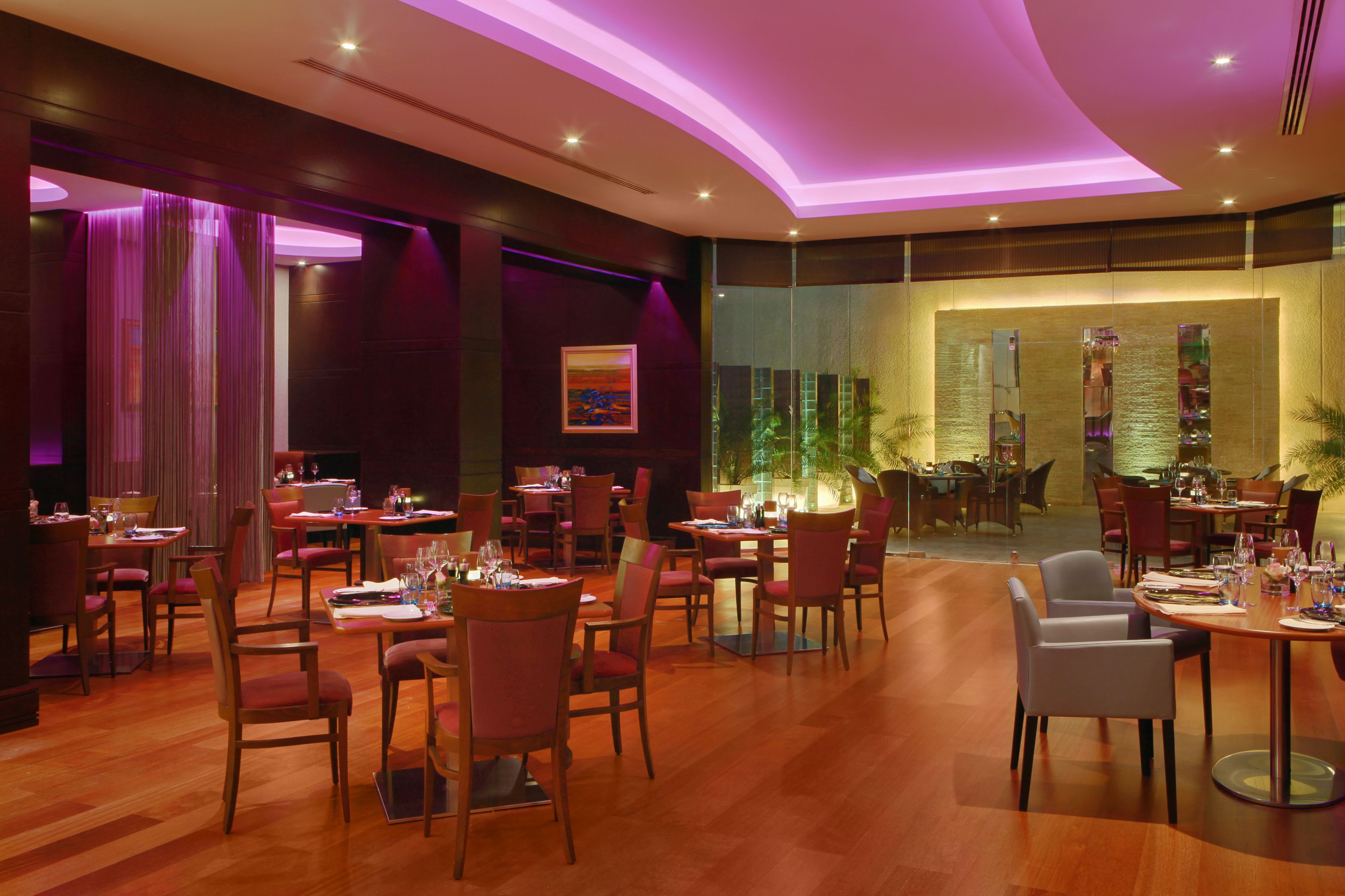 A restaurant with wooden flooring, tables set with red chairs, and a view of the dining area through a glass wall.