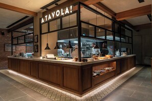 Un espace cuisine moderne avec un comptoir en bois et une grande fenêtre donnant sur les chefs en pleine activité.