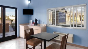 A compact kitchen with a dining area, a flat-screen TV, and a window with blinds. - Travelodge by Wyndham Banning CA Near Casino/Outlet Mall (Banning)