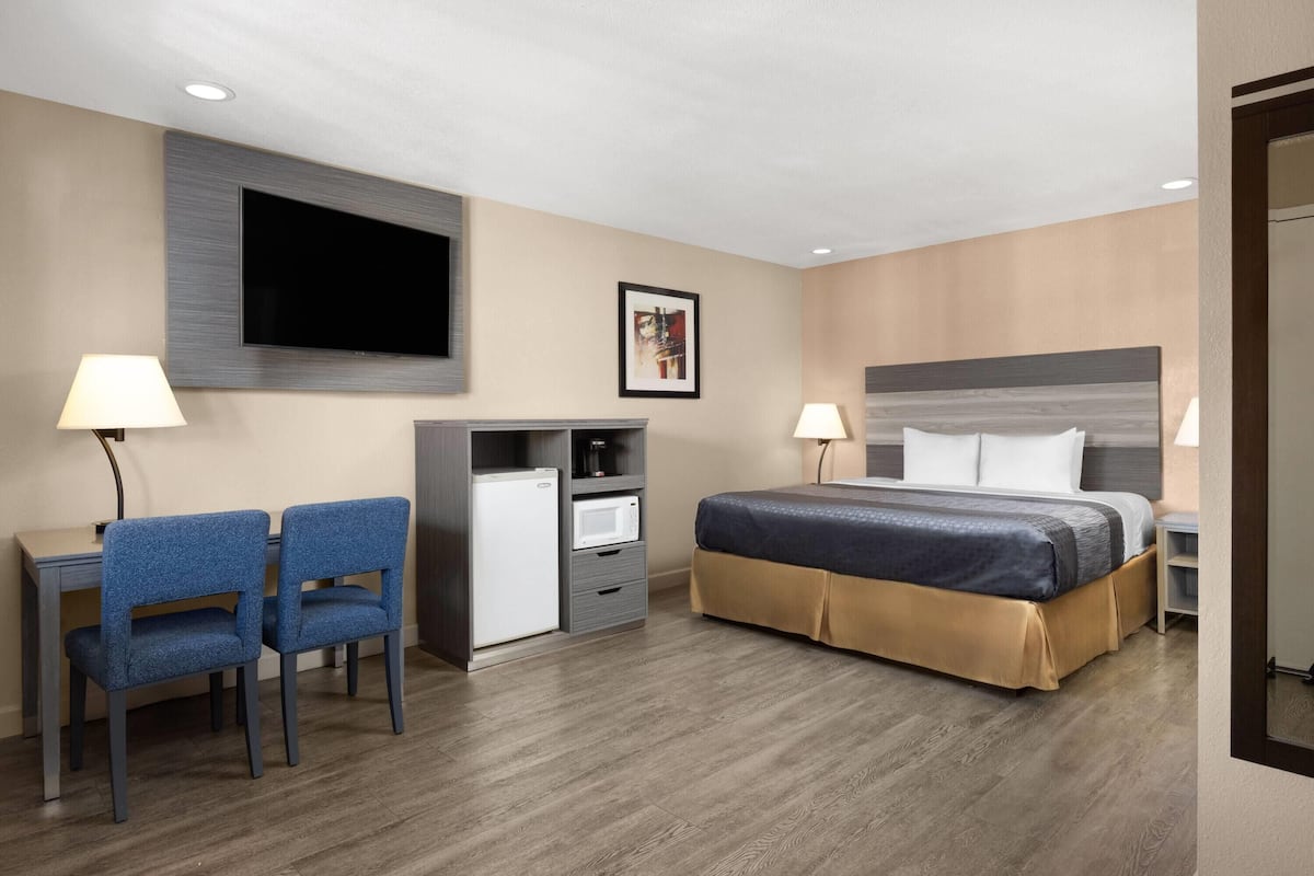 A hotel room with a bed, desk, chairs, a TV, and a microwave.