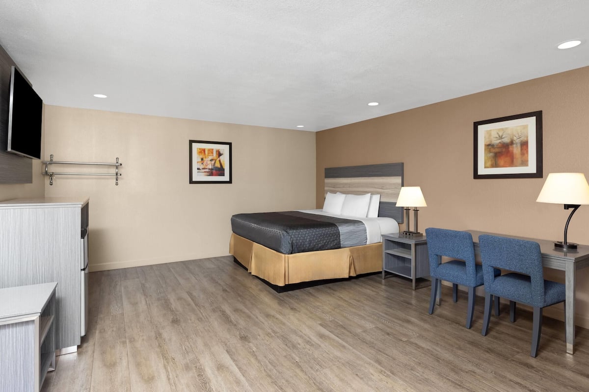 A hotel room with a bed, desk, chairs, and artwork on the walls.