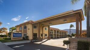 A Travelodge hotel with a clear sign, a covered parking area, and a view of mountains in the background. - Travelodge by Wyndham Banning CA Near Casino/Outlet Mall (Banning)