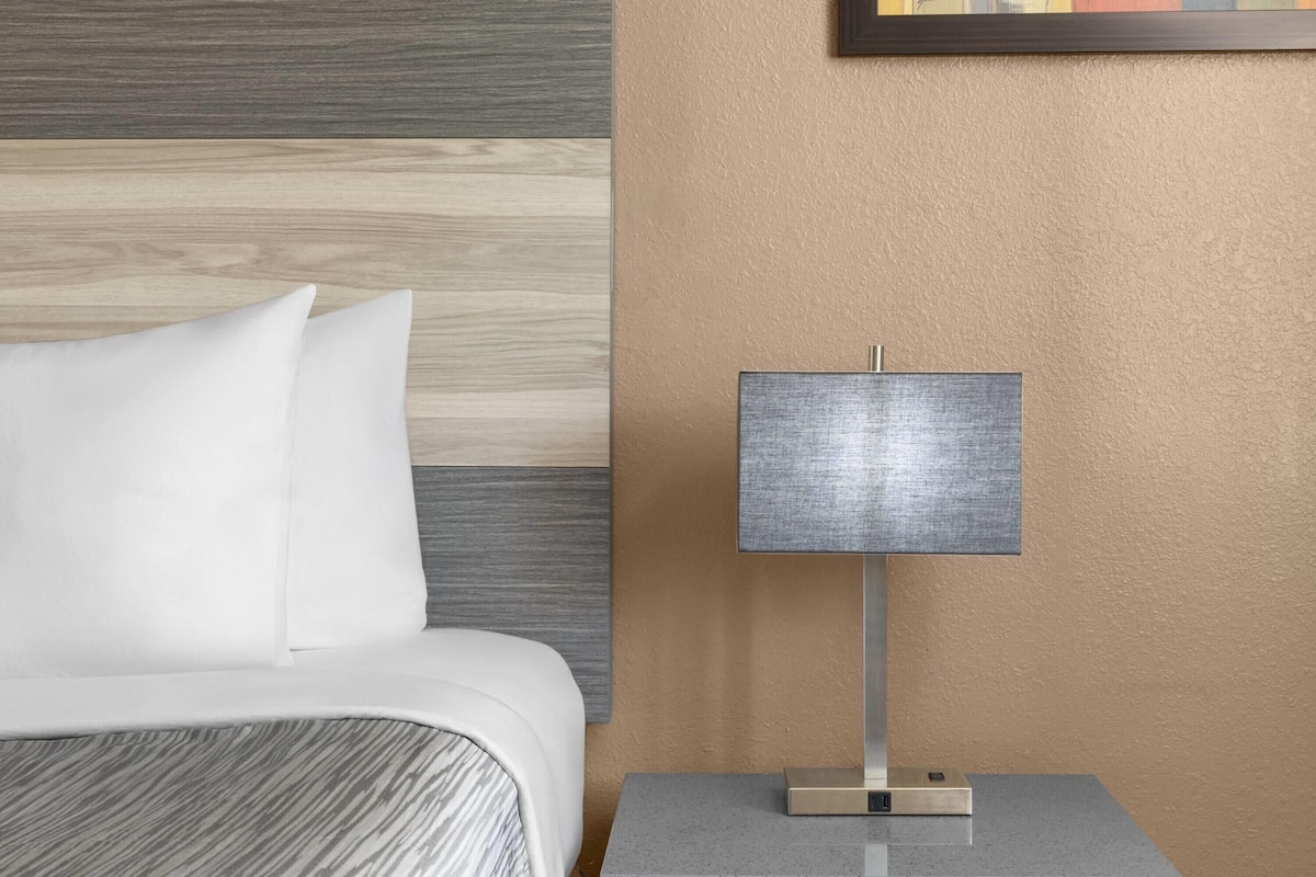 A hotel room with a bed, a nightstand, and a lamp.