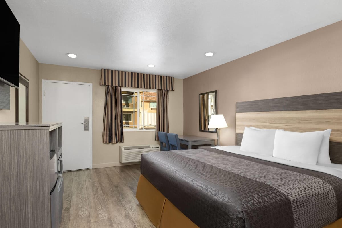A hotel room with a bed, desk, chair, and a view of the outside.