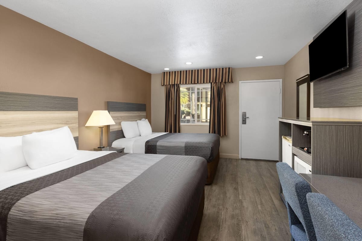 A hotel room with two beds, a TV, a desk, and a window with curtains.