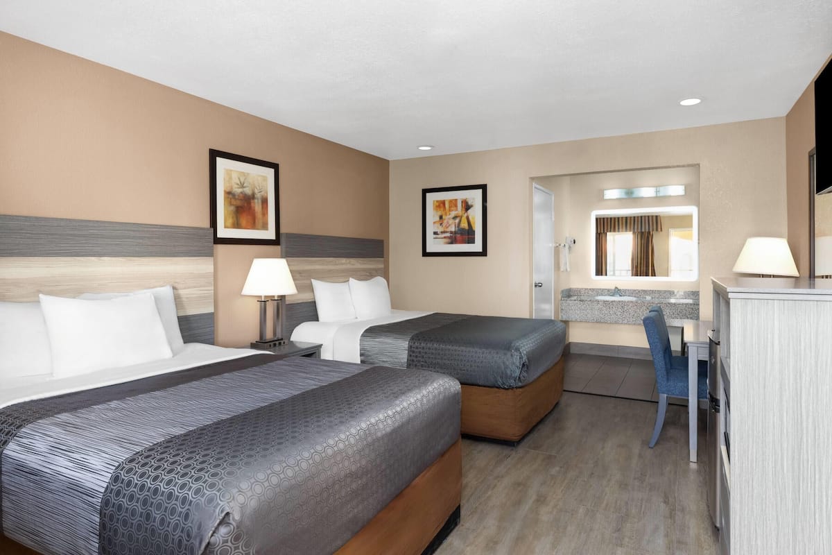 A hotel room with two beds, a desk, a chair, and a bathroom mirror.