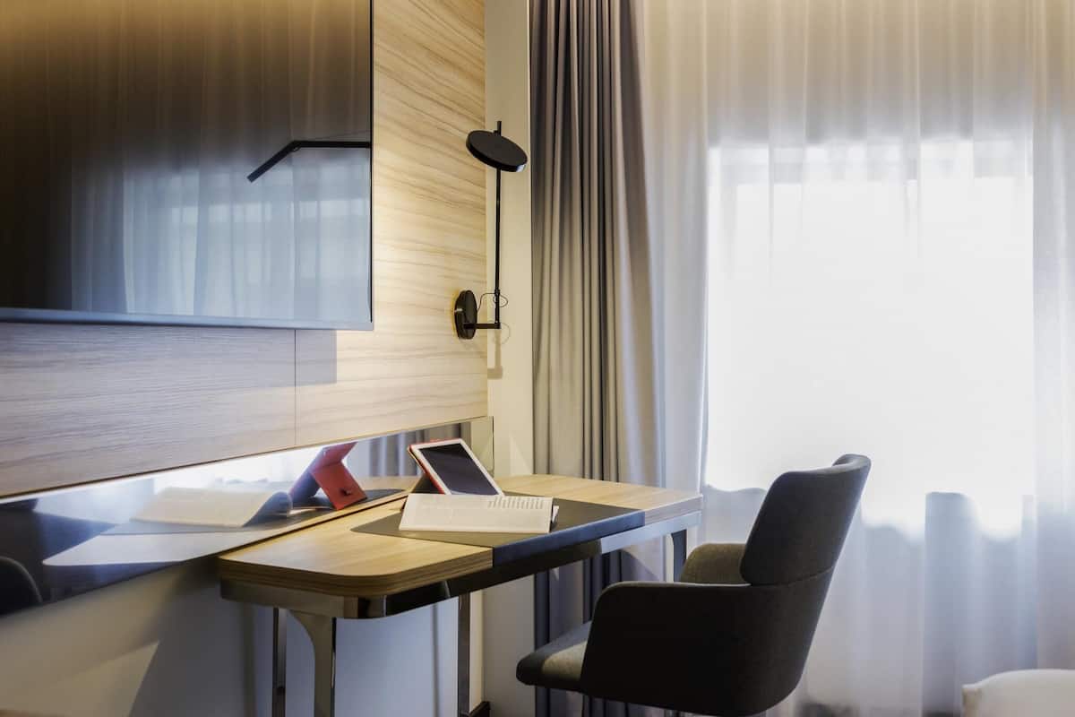 Une chambre dâhĂŽtel moderne avec un bureau en bois, un ordinateur portable, une tablette et une chaise.