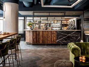 A modern bar area with a wooden counter, marble backsplash, and a variety of bottles and glasses. - Novotel Den Haag City Centre (The Hague)