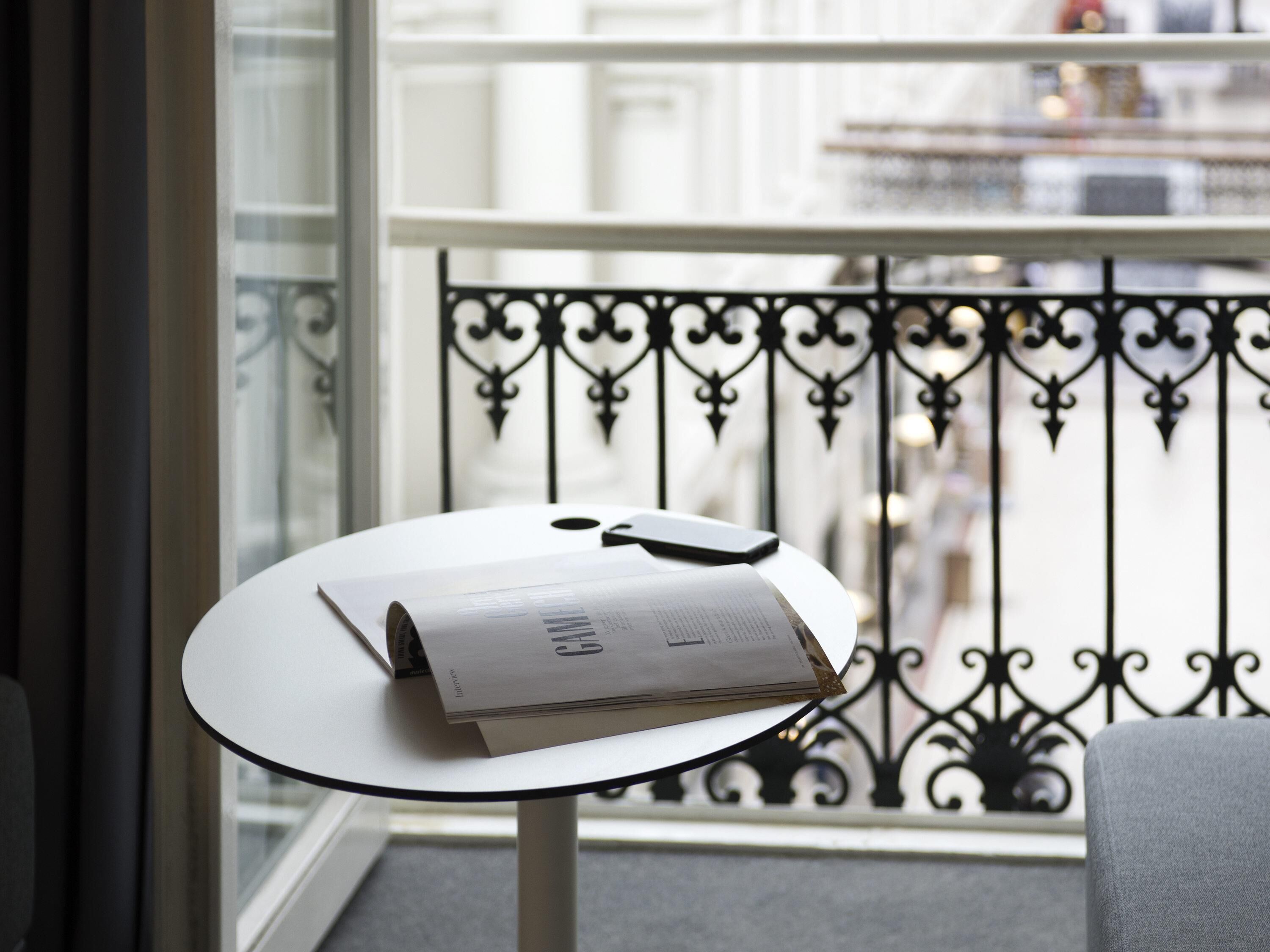 A small round table with a magazine and a smartphone on it, a balcony railing, and a view of the street.