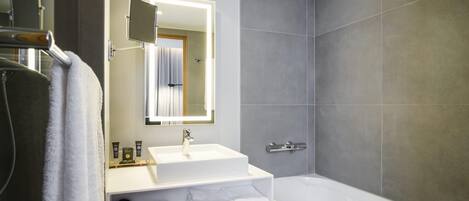 A modern bathroom with a white sink, a mirror, a bathtub, and grey tiles.