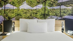 Ein modernes Hotelzimmer mit einem großen Bett, weißen Kissen und einer Wandmalerei mit geometrischem Muster.