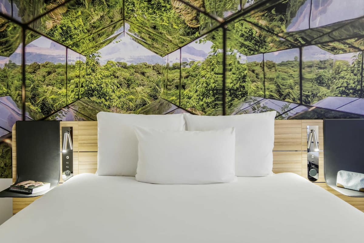 Una habitación de hotel moderna con una cama grande, almohadas blancas y un mural de pared con diseño geométrico.