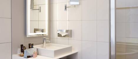 Une salle de bain moderne avec un grand miroir, un lavabo blanc et un porte-serviettes.