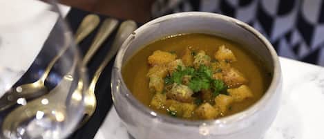 A bowl of soup with croutons and parsley garnish on a marble table.