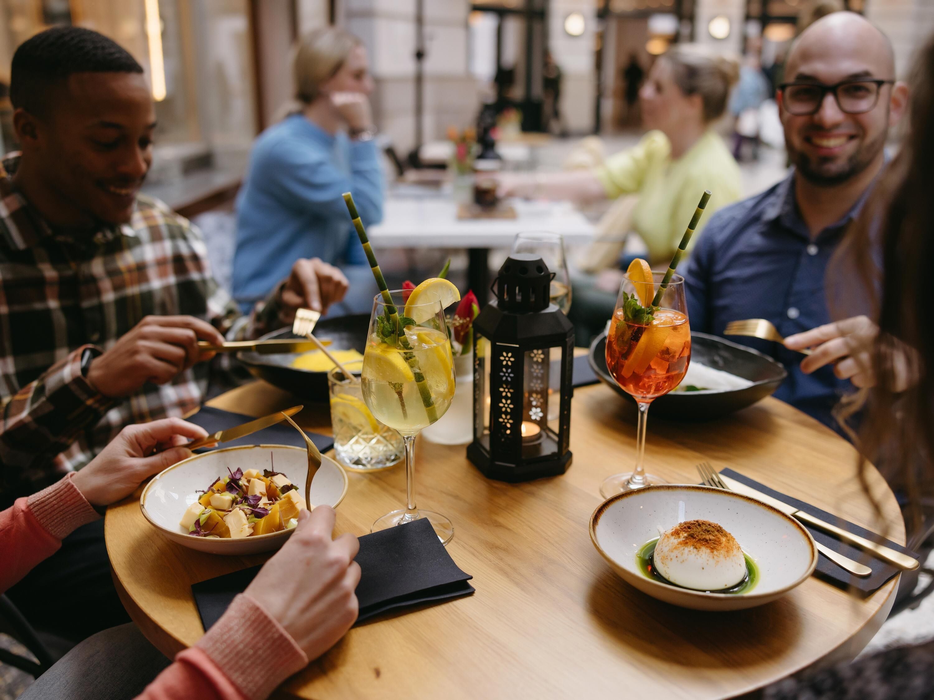 Een groep mensen dineert aan een ronde tafel met verschillende gerechten en drankjes.