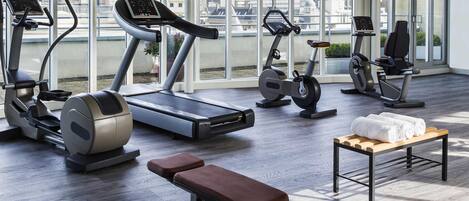 Una palestra moderna con diverse macchinette per esercizi cardio, una panca e un piccolo tavolo con asciugamani.
