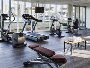 Un gimnasio moderno con diferentes máquinas de cardio, una banca y una pequeña mesa con toallas.