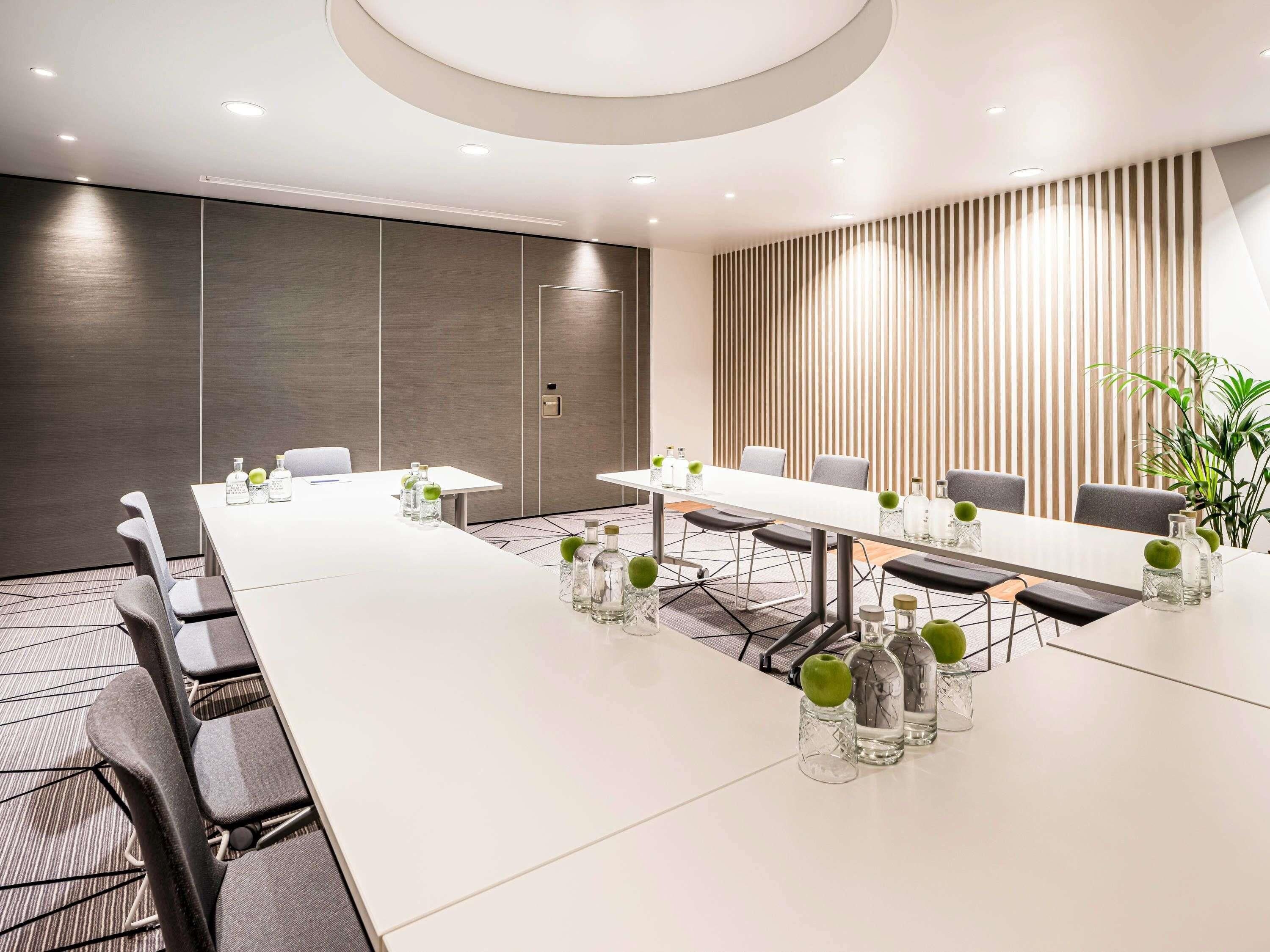 A conference room with a long table, chairs, and glass vases with green apples.