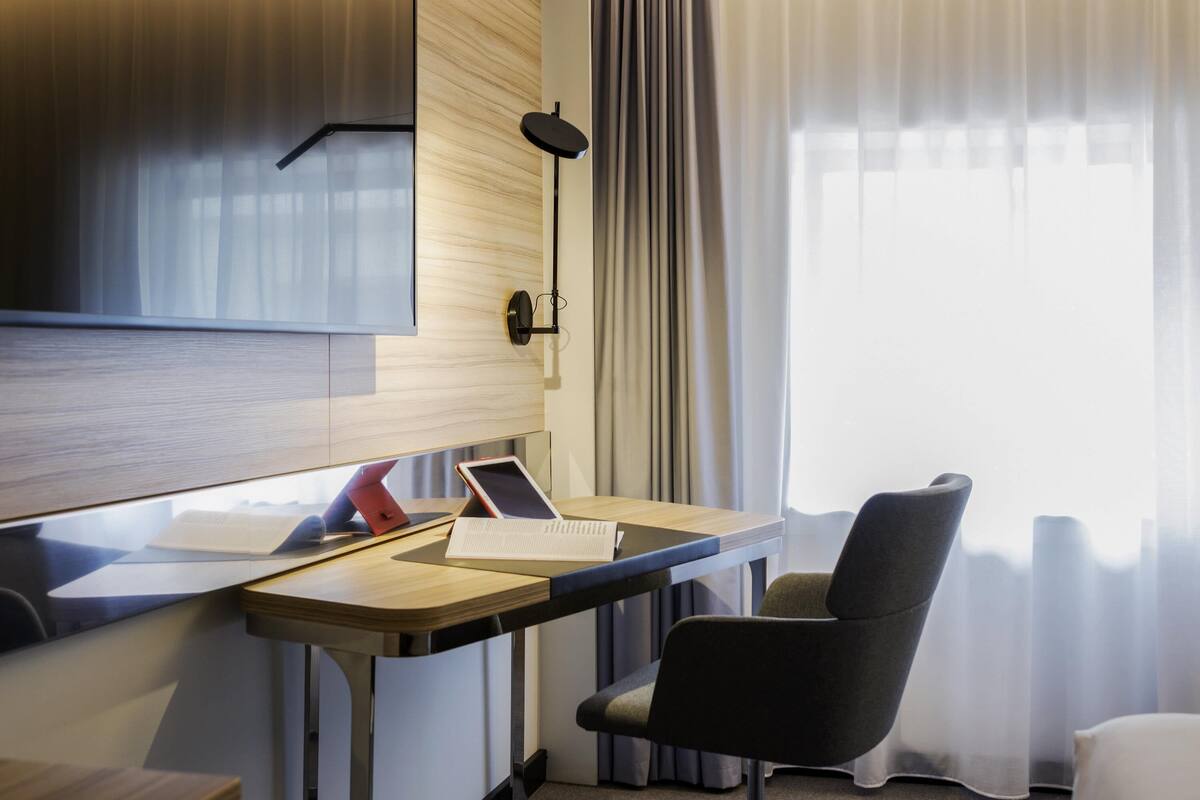 Een moderne hotelkamer met een houten bureau, een laptop, een tablet en een stoel.
