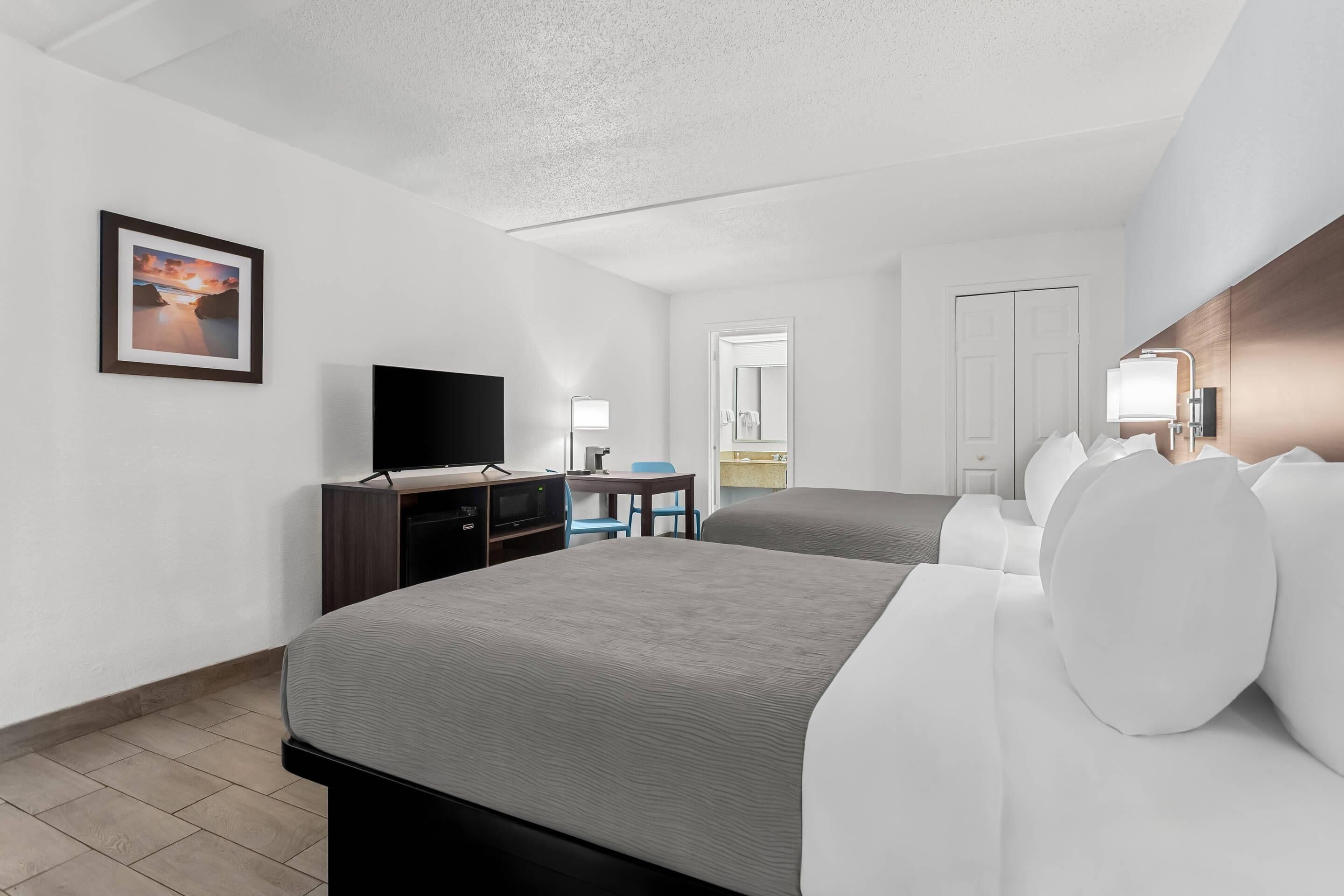 A hotel room with a large bed, a desk with a computer, a TV, and a framed picture on the wall.