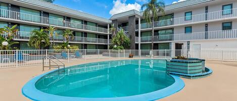 Un hotel con piscina, varios balcones y plantas tropicales.