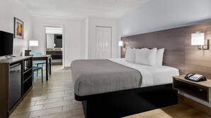 Habitación de hotel con cama, mesita de noche con teléfono, escritorio con lámpara, silla y televisor.