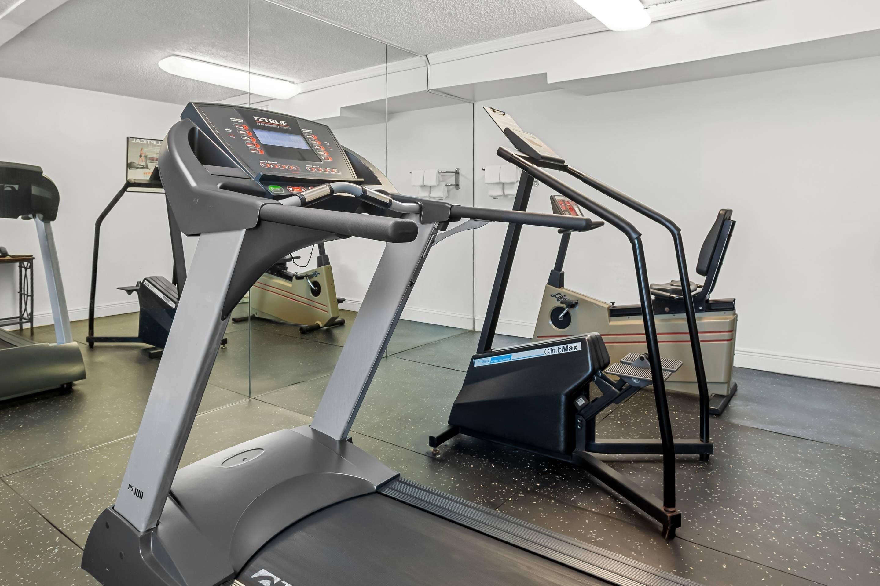 Academia com esteiras, simulador de escada e banco de musculação.