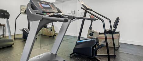 Academia com esteiras, simulador de escada e banco de musculação.