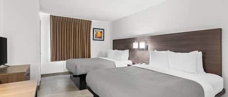 A hotel room with two beds, a desk, a TV, and a window with curtains.