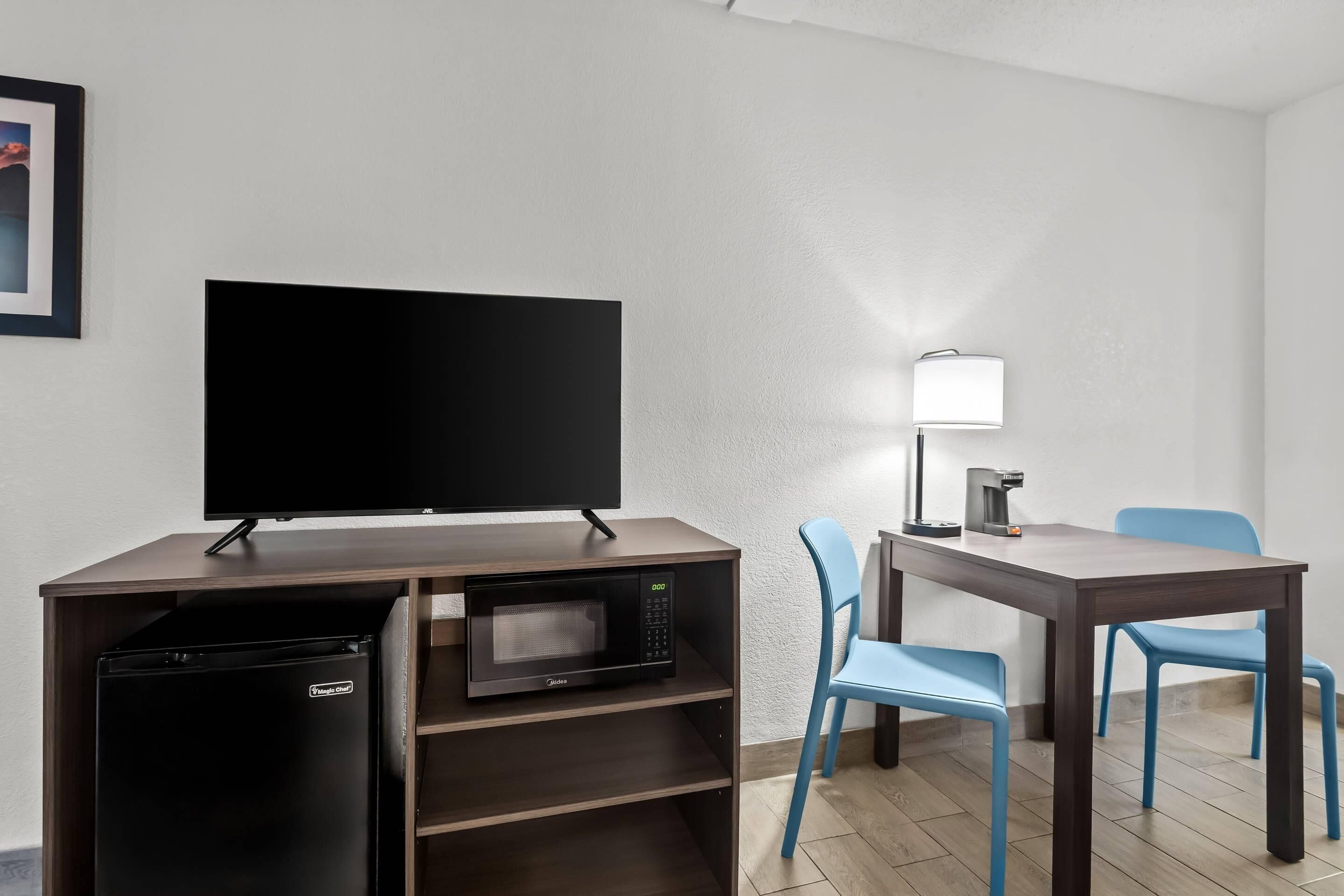 Habitación con televisión de pantalla plana, microondas, cafetera y una mesa con sillas.