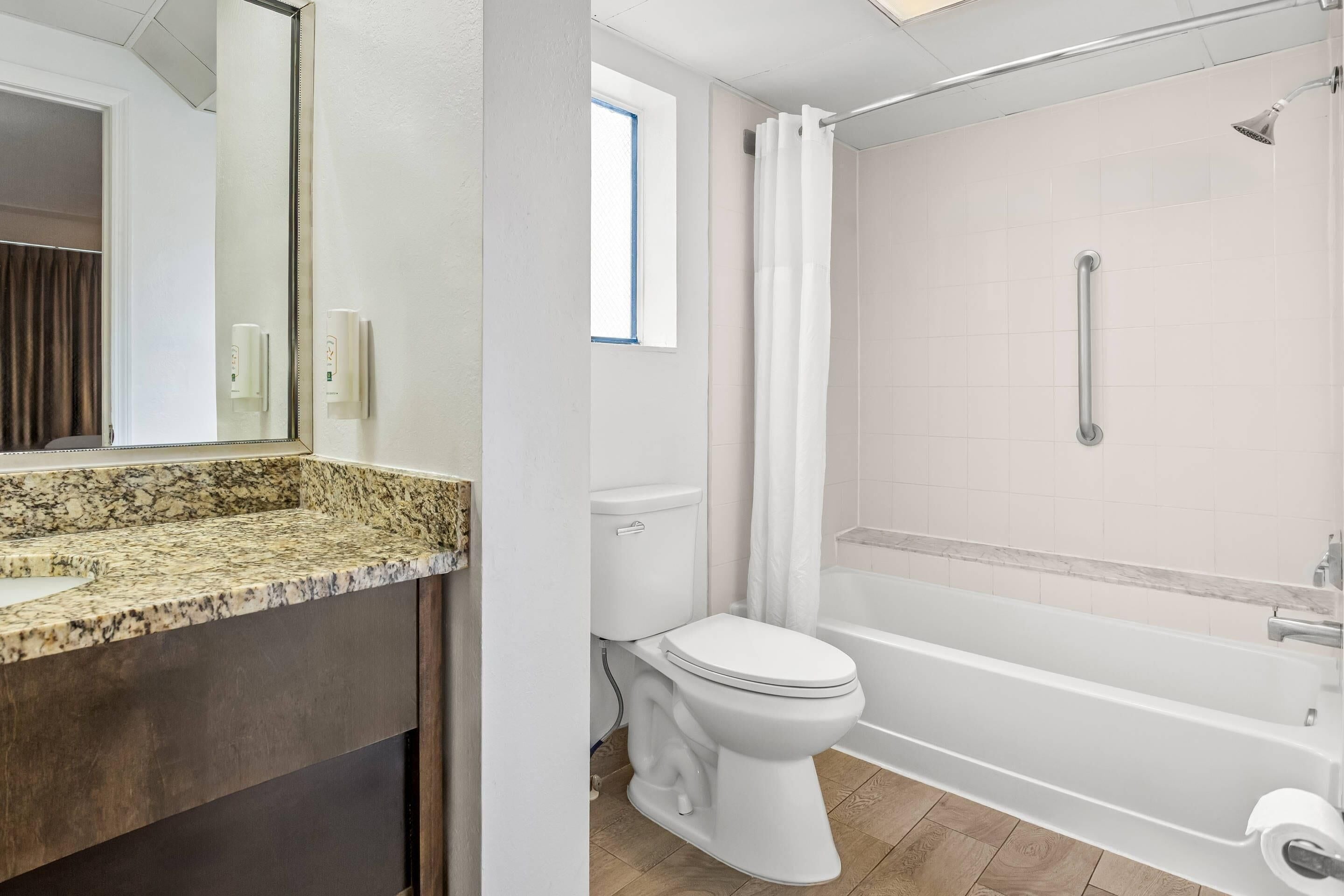 A bathroom with a marble countertop, a toilet, a bathtub, and a shower.