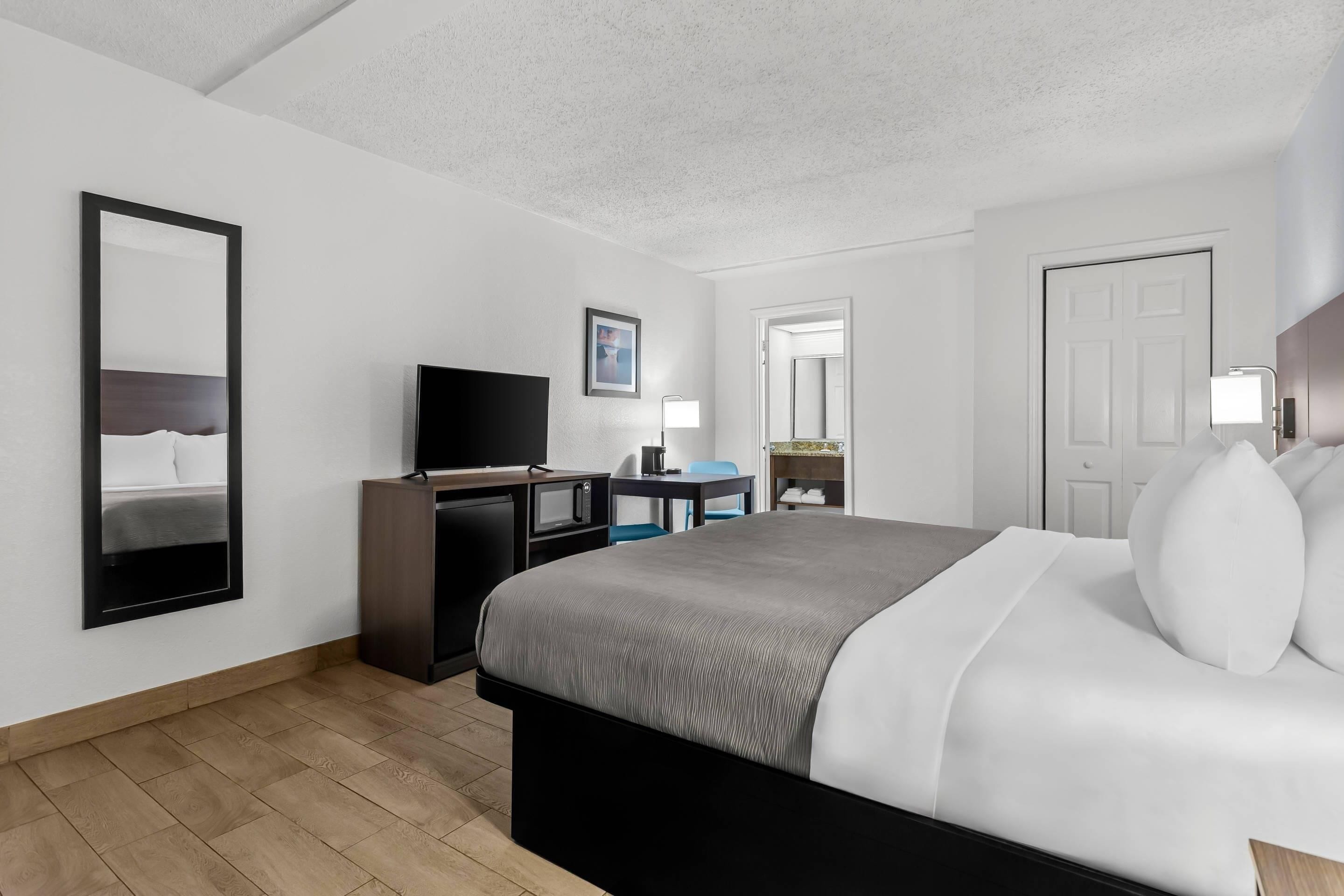 Una habitación de hotel moderna con una cama grande, un escritorio con un televisor de pantalla plana, una lámpara de escritorio y un espejo.