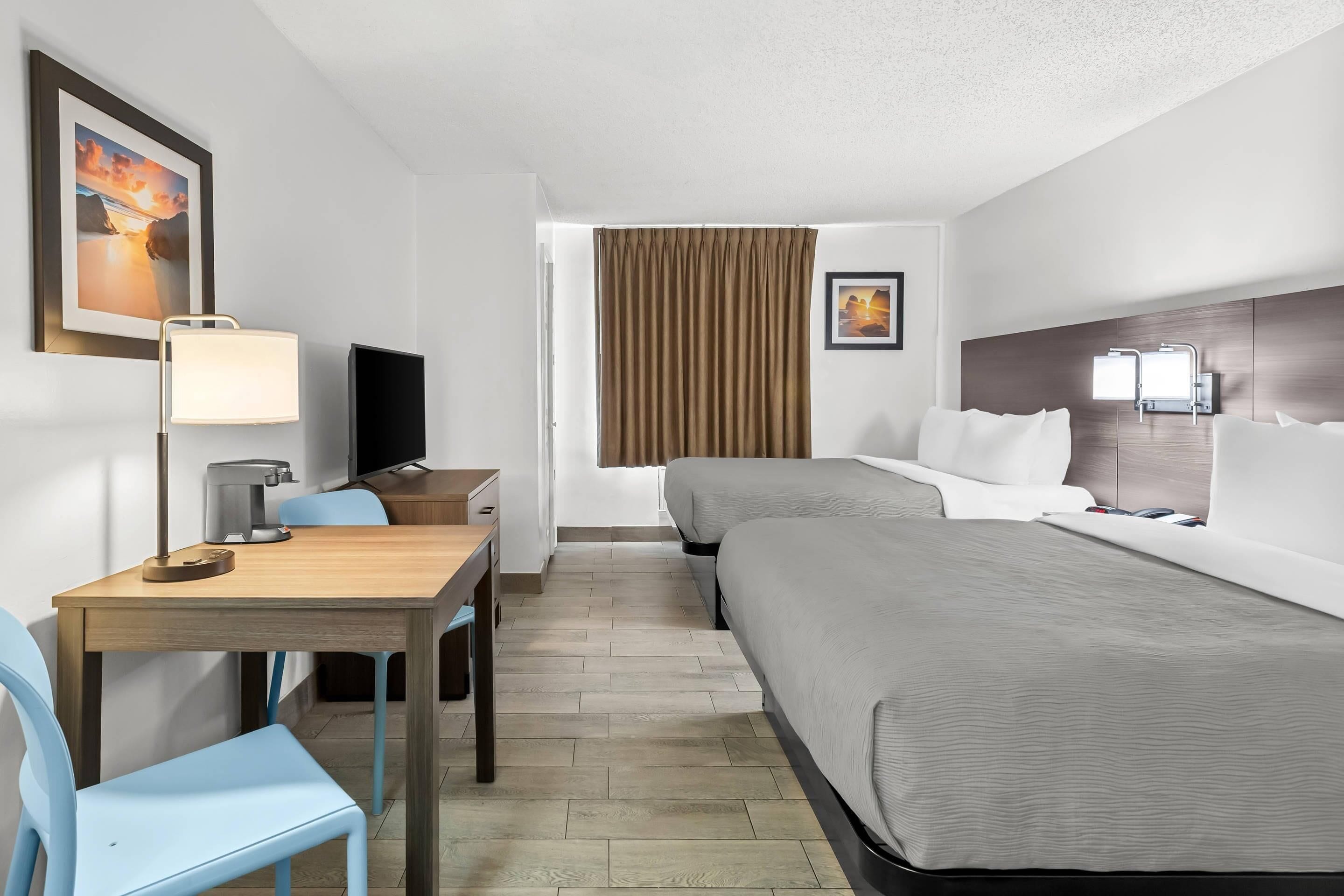 Une chambre d’hôtel avec un lit, un bureau avec une lampe, une chaise, un téléviseur et une fenêtre avec des rideaux.