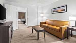 Una sala moderna con un sofá de cuero marrón, una mesa de centro de madera, un televisor sobre un mueble de madera y un cuadro en la pared.