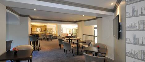 Un hall d’hôtel comprenant un bar, des espaces aménagés avec des sièges et un téléviseur fixé au mur.