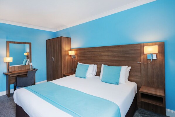 A hotel room with a large bed, a wooden wardrobe, a desk with a chair, and two wall-mounted lamps. - The Bromley Court Hotel (Bromley)