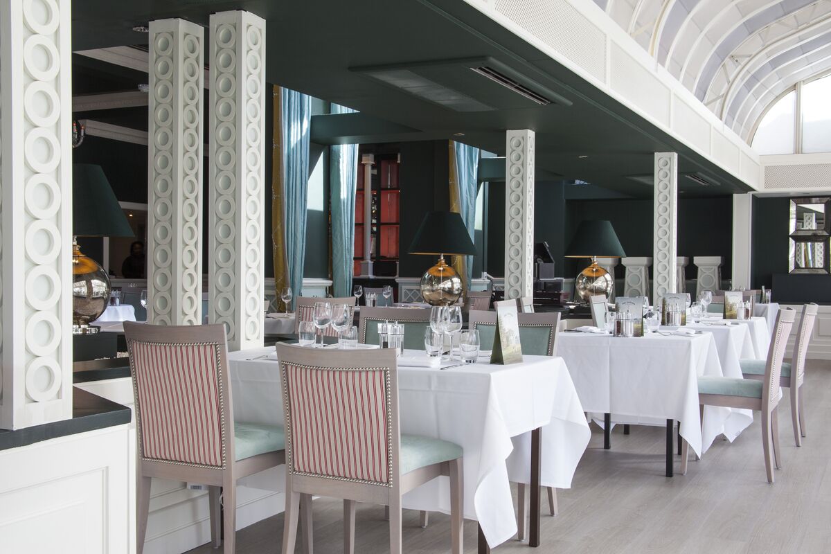 A formal dining area with white tables and chairs, large decorative columns, and a high ceiling with a skylight.