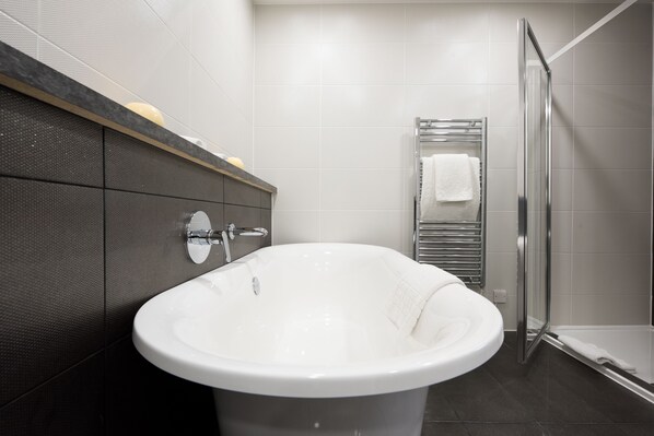 A modern bathroom with a freestanding bathtub, a glass shower enclosure, and a chrome towel rack. - The Bromley Court Hotel (Bromley)