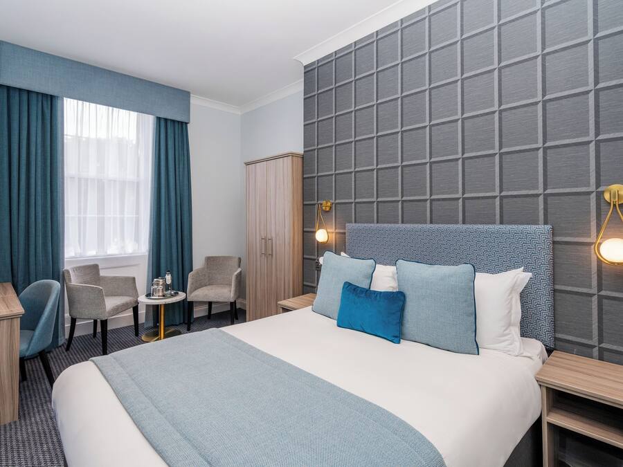 Ein Hotelzimmer mit einem großen Bett, zwei Sesseln, einem Schreibtisch und einem Kleiderschrank.
