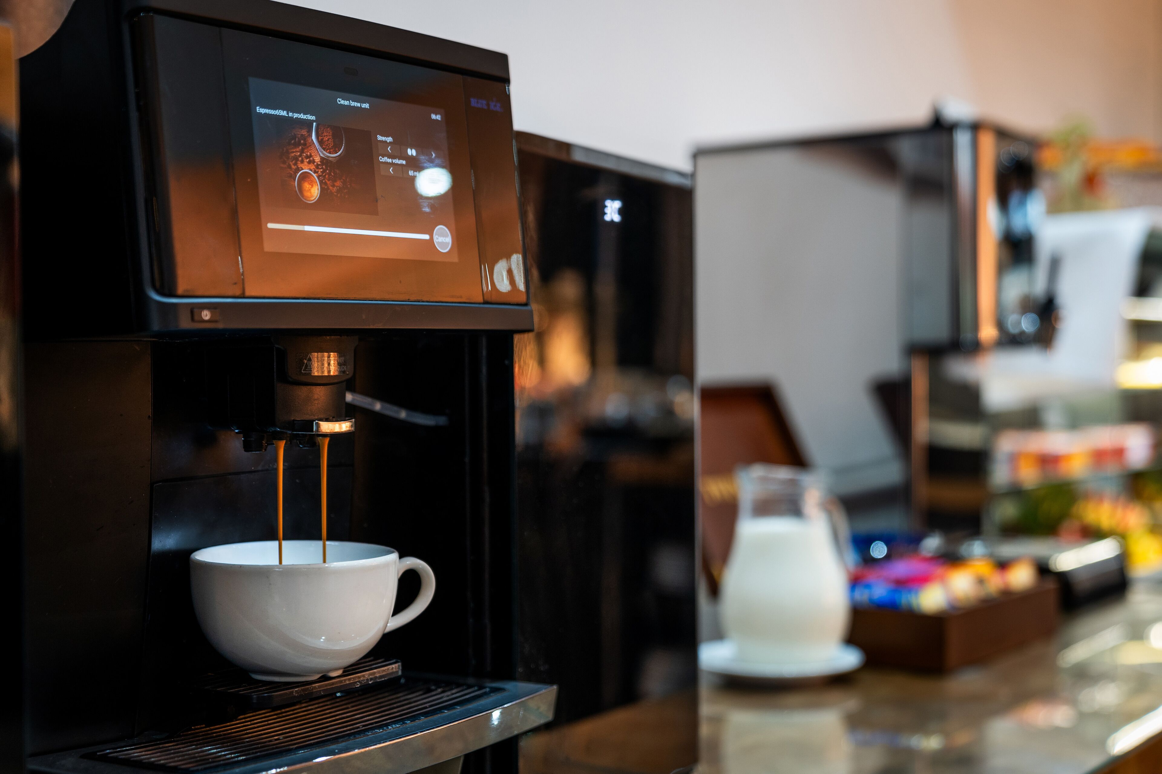 A coffee machine with a digital display, a white cup, and a milk jug on a counter.