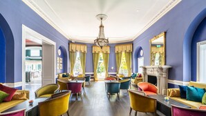 A spacious room with a fireplace, multiple seating areas, and a large mirror on one wall. - The Bromley Court Hotel (Bromley)
