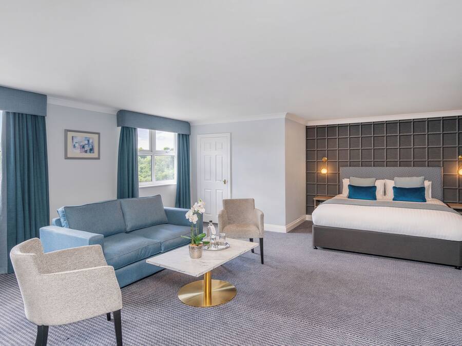 A hotel room with a bed, a sofa, a chair, a coffee table, and a view of the outdoors.