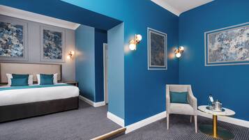 Una habitación de hotel con una cama grande, una silla, una mesita y obras de arte en las paredes.