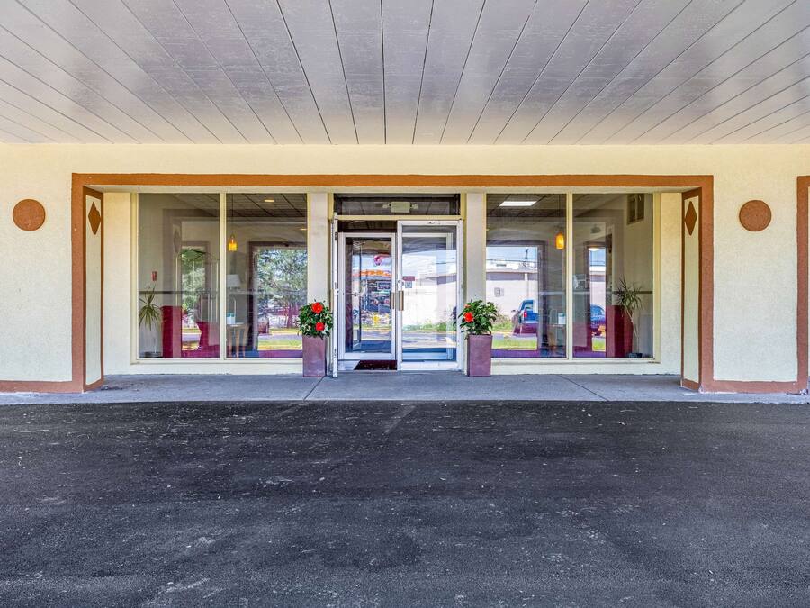 A hotel entrance with a glass door, potted plants, and a parking lot.