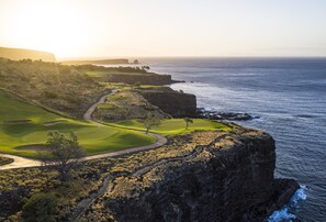 A coastal golf course with a clear path, a water body, and a rocky cliff.