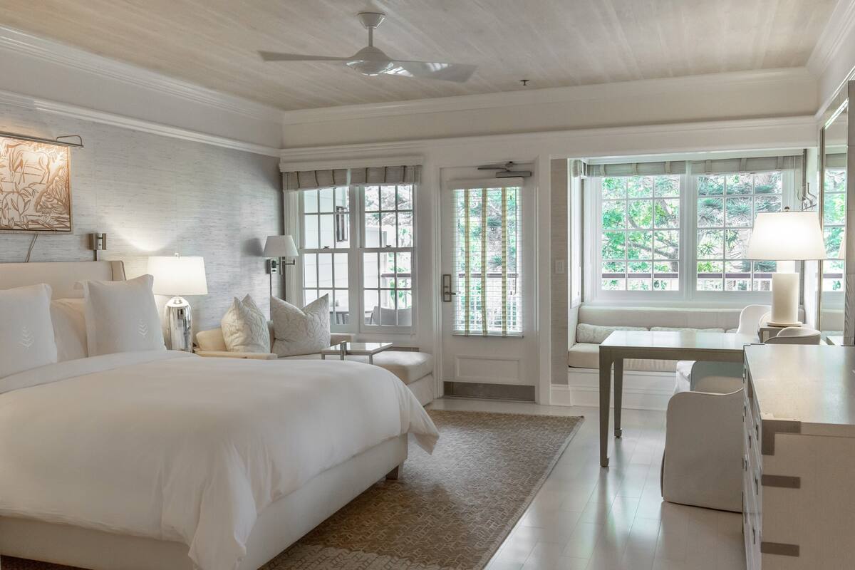 A spacious bedroom with a large bed, a desk, and a seating area by the window.