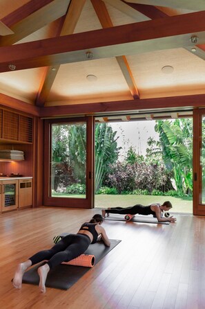 A spacious room with wooden floors, large sliding glass doors leading to a garden, and a ceiling with exposed beams.